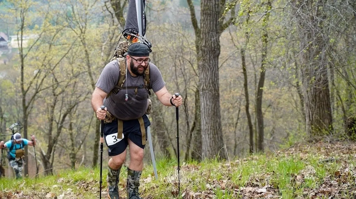 A man hiking through a forested trail wearing a backpack and cap.